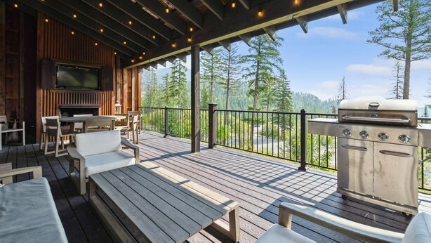A wooden deck with outdoor seating, a barbecue grill, and a television mounted on a wooden wall.