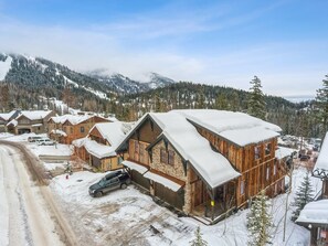 Un bâtiment de style chalet en bois, doté d’un toit à forte pente, entouré d’arbres couverts de neige et avec des montagnes en arrière-plan.