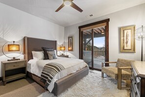 Une chambre avec un grand lit, deux lampes de chevet, une tête de lit en bois, un bureau avec une chaise et une vue sur l’extérieur à travers une porte vitrée.