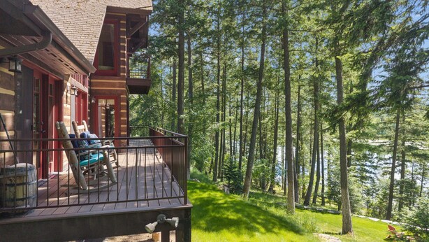 Een houten terras met stoelen, een klein tafeltje en uitzicht op een bos en meer.