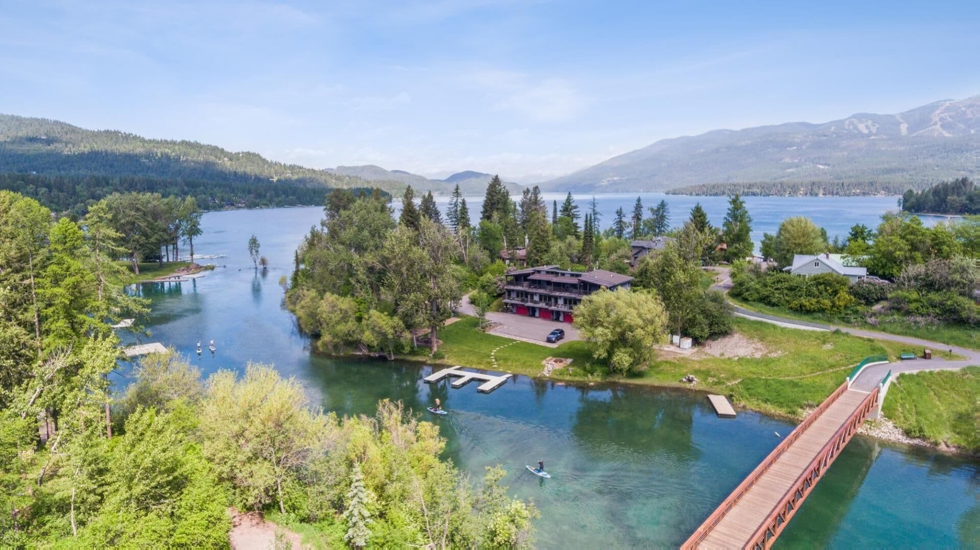 A lakeside property with a dock, a building with a red roof, and a bridge.