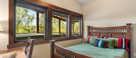 A bedroom with a large window, wooden headboard, and a green quilted bedspread.