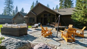 A wooden cabin with a stone patio, outdoor seating, and a large fireplace. - Mountain Home with Private Hot Tub (Columbia Falls)