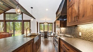 A modern kitchen with wooden cabinets, a large island, and a view of the outdoors. - Mountain Home with Private Hot Tub (Columbia Falls)