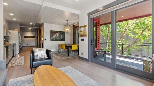A modern interior with a dining area, kitchen, and a balcony with a red railing.