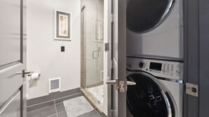 A laundry room with two stacked washing machines, a glass door, and a framed picture on the wall.