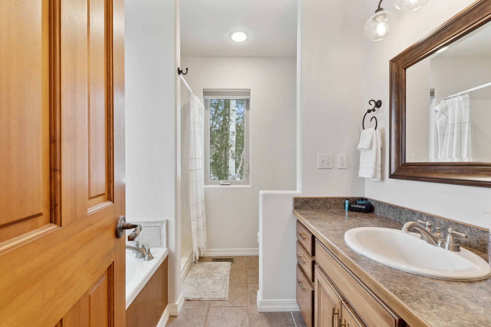 A bathroom with a wooden vanity, a large mirror, and a window providing natural light.