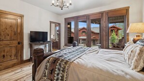 A bedroom with a large bed, a television, a wooden door, and a view of a house through a large window. - Ski-in/Ski-out Access and Private Hot Tub (Whitefish)