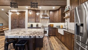 Une cuisine moderne avec des meubles en bois, un grand îlot central, des appareils en acier inoxydable et des luminaires suspendus.