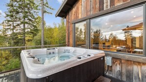 Un bain à remous sur un balcon, avec une structure extérieure en bois et de grandes fenêtres qui reflètent un paysage boisé.