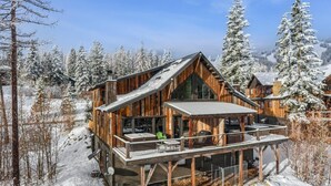 Une cabane en bois dotée d’une terrasse et de grandes fenêtres, entourée d’arbres couverts de neige.
