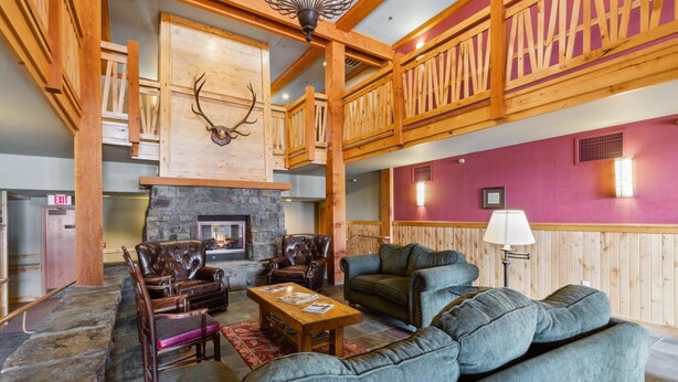 A lobby with a stone fireplace, leather armchairs, a blue sofa, and wooden paneling.