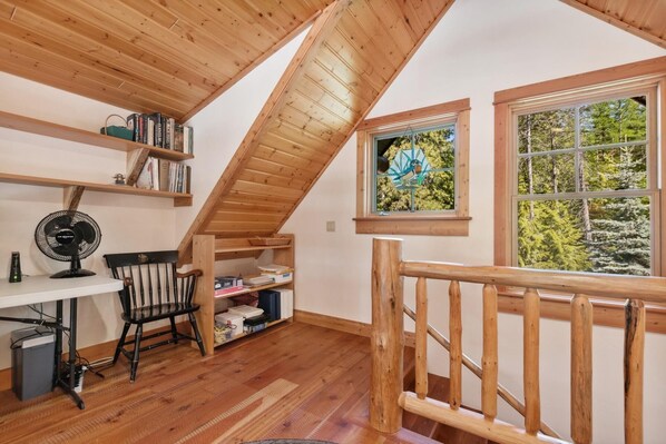 A cozy attic room with wooden beams, a desk with a chair, a fan, and bookshelves. - Mountain and Forest Views with Fireplace (Whitefish)