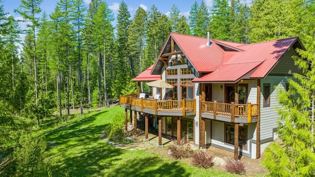 A two-story log cabin with a red roof, wooden deck, and large windows.