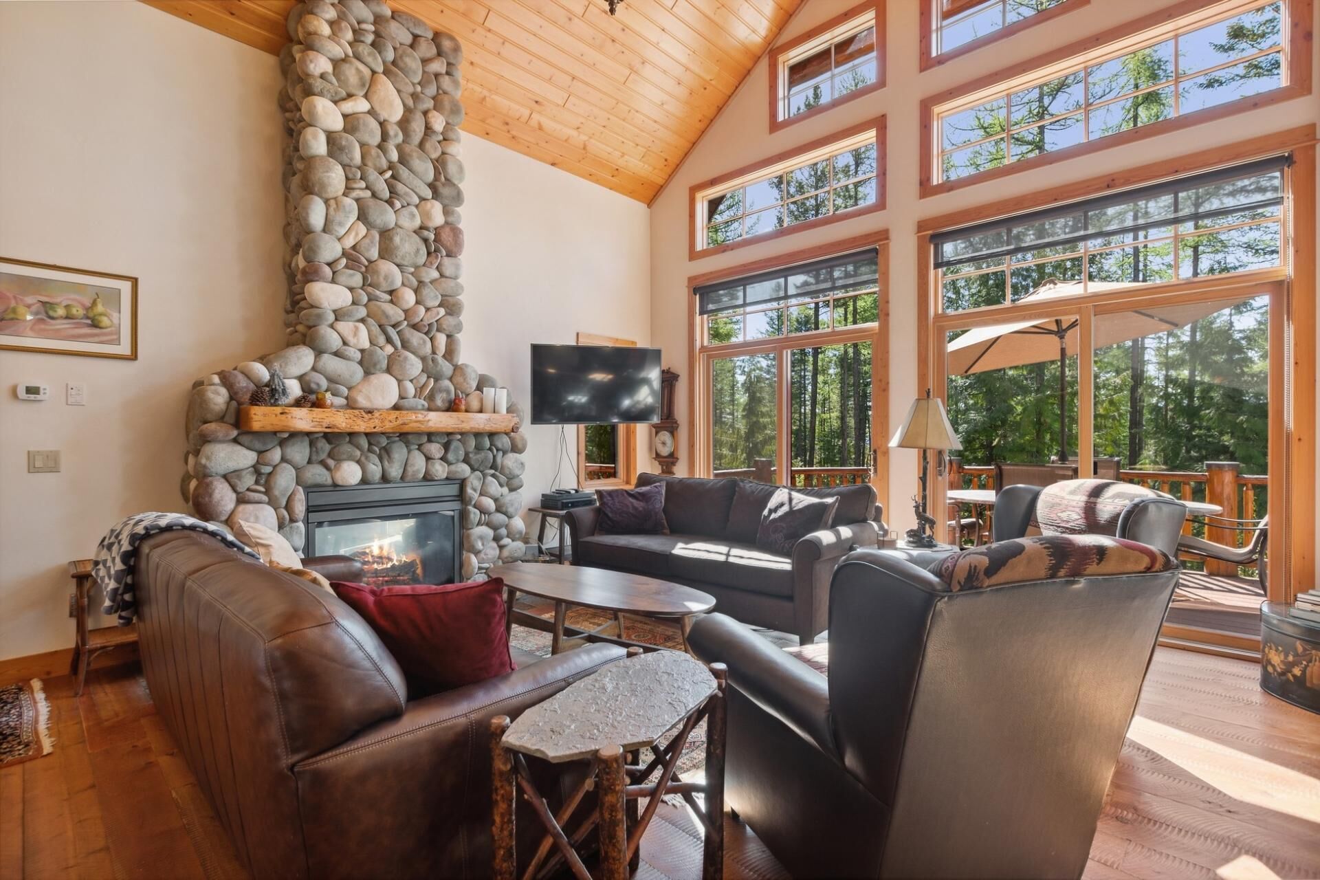 Un salon chaleureux avec une cheminée en pierre, des meubles en cuir et de grandes fenêtres donnant sur la forêt.