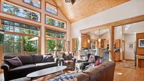 A spacious living room with a large window, a wooden ceiling, and a cozy seating area.