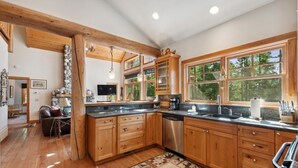 A spacious kitchen with wooden cabinets, a stainless steel dishwasher, and large windows offering a view of the outdoors.