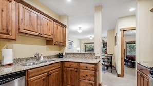 A kitchen with wooden cabinets, granite countertops, a dishwasher, and a dining area with a table and chairs.