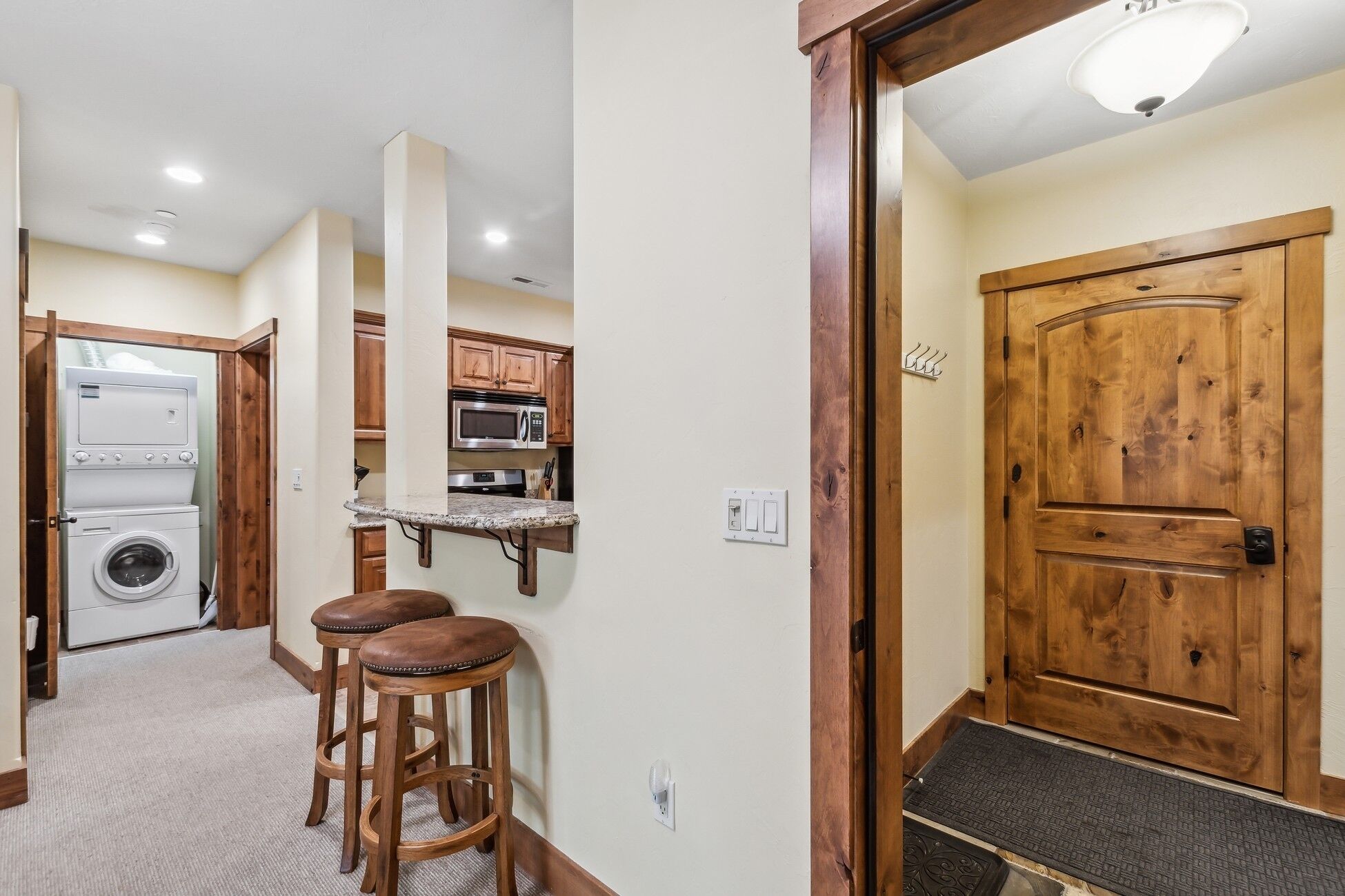 A compact kitchen with a washing machine, a microwave, and wooden bar stools.