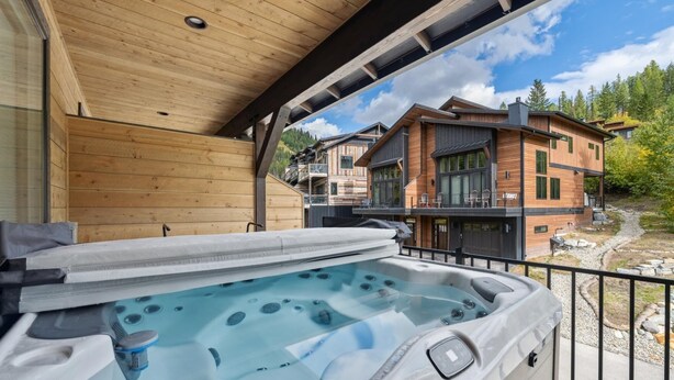 A hot tub on a balcony with a view of a wooden building and a forest.