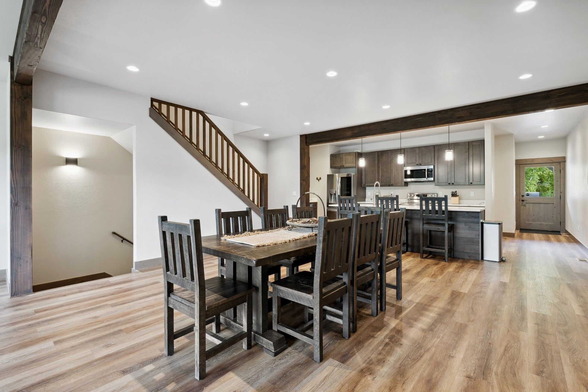 Un vaste espace de salle à manger avec une table et des chaises en bois, une cuisine équipée d’appareils modernes et un escalier menant à un autre niveau.