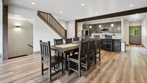 A spacious dining area with a wooden table and chairs, a kitchen with modern appliances, and a staircase leading to another level.