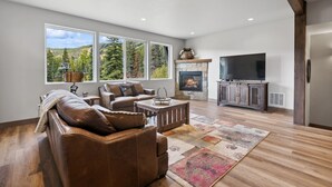 A spacious living room with a fireplace, large windows, and a flat-screen TV.