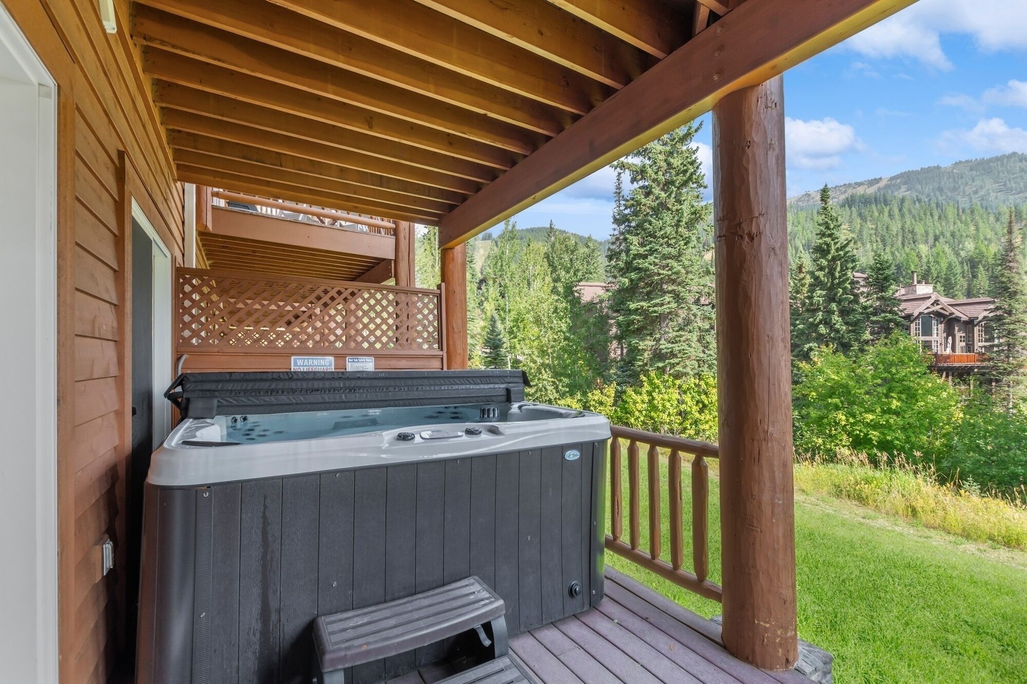 Een houten terras met een jacuzzi en een bankje, met uitzicht op een bebost dal.