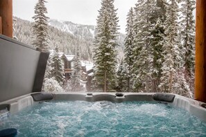 Een hottub met uitzicht op besneeuwde bomen en gebouwen.