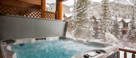 A hot tub on a balcony with a view of snow-covered trees and buildings.
