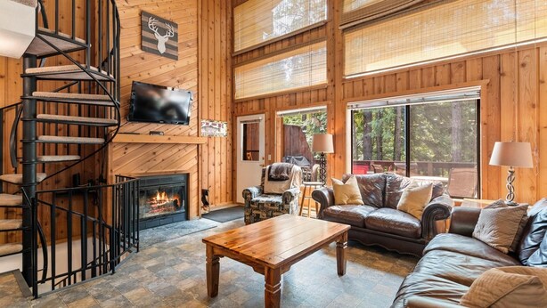 A spacious living room with a fireplace, a wooden staircase, and large windows. - 15 Mins to Downtown w/ Shared Hot Tub (Whitefish)