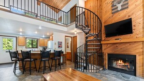 A spacious living area with a wooden staircase, a fireplace, and a TV mounted on the wall. - 15 Mins to Downtown w/ Shared Hot Tub (Whitefish)
