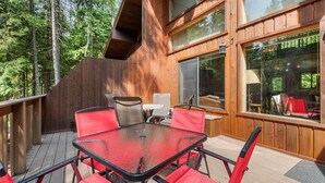 A wooden deck with a glass table and red chairs, surrounded by a forest. - 15 Mins to Downtown w/ Shared Hot Tub (Whitefish)