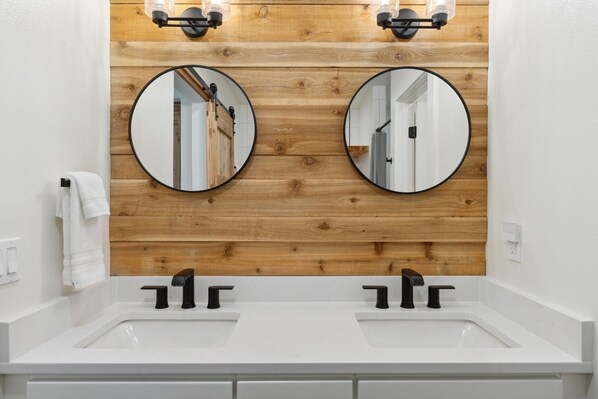 A bathroom with two sinks, wooden panel wall, and two round mirrors. - Loft Space | Dogs Welcome | Amenities (Whitefish)