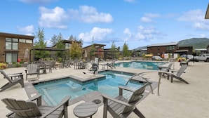 A pool area with lounge chairs and tables, surrounded by buildings and trees. - Mountain Views and Clubhouse Access (Whitefish)