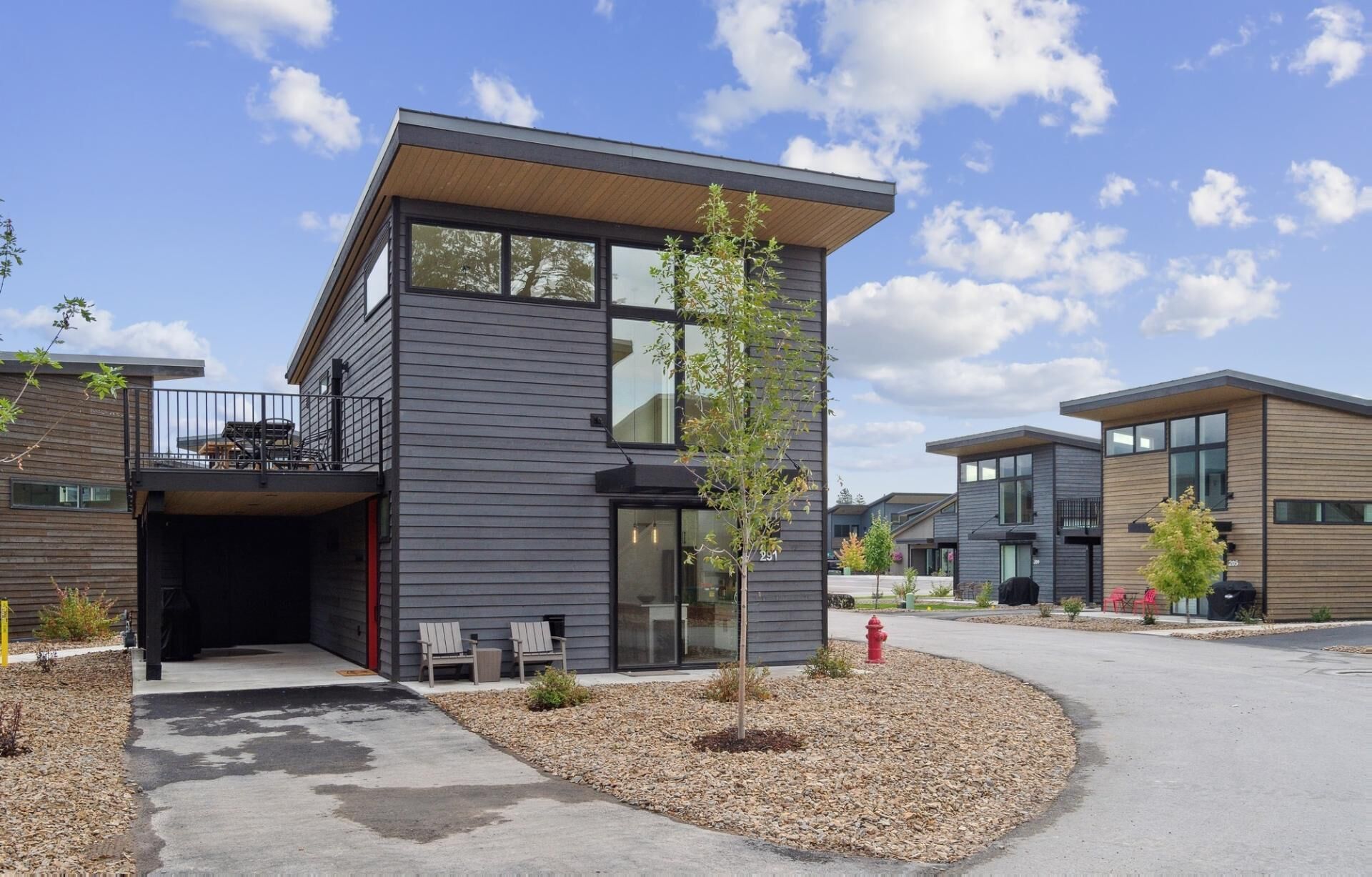 Een modern gebouw met twee verdiepingen, een plat dak, grote ramen en een kleine boom in de voortuin.