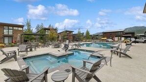 A pool area with lounge chairs and tables, surrounded by buildings and trees.