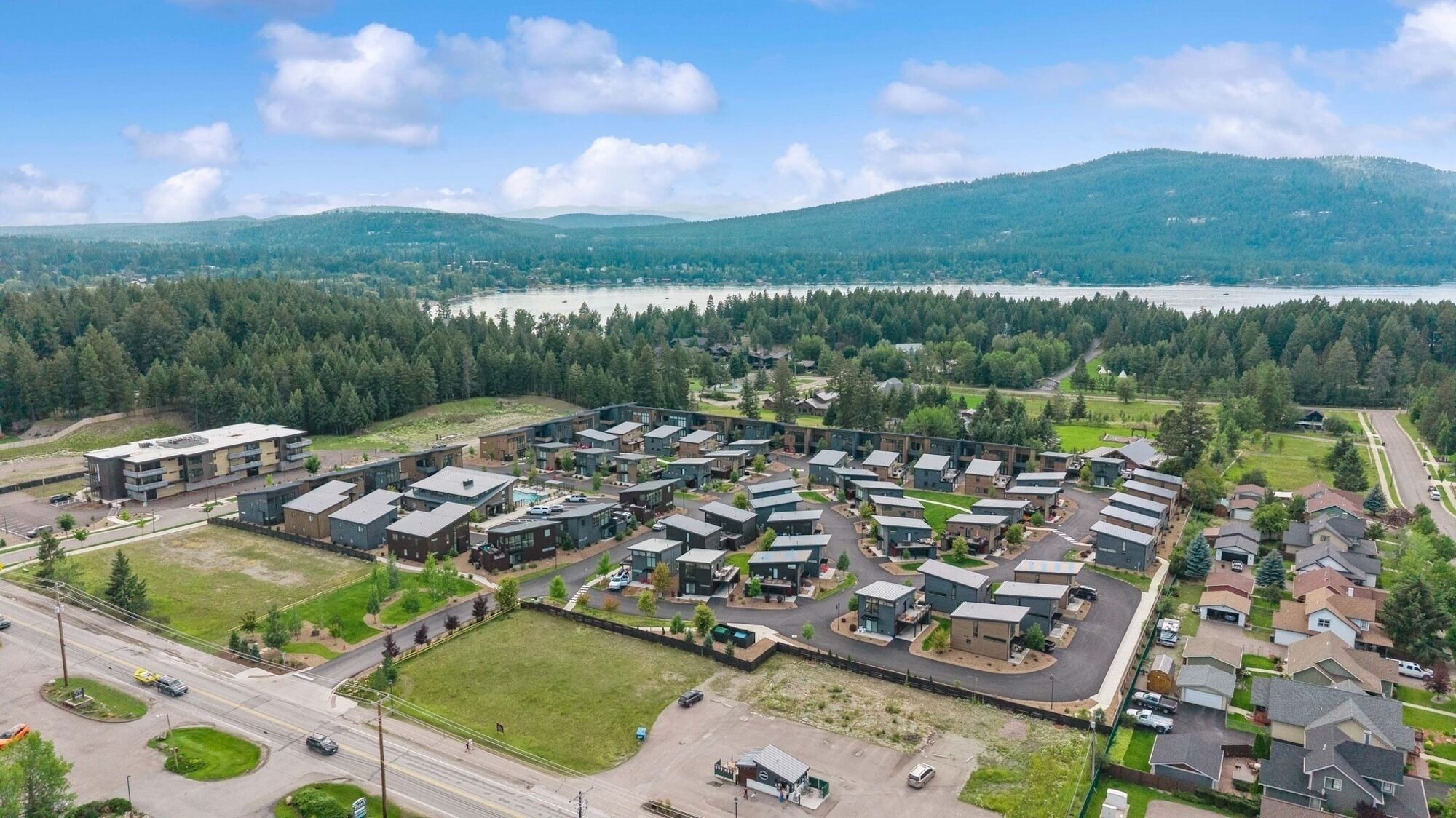 A residential area with modern houses, a central road, and a lake in the background.