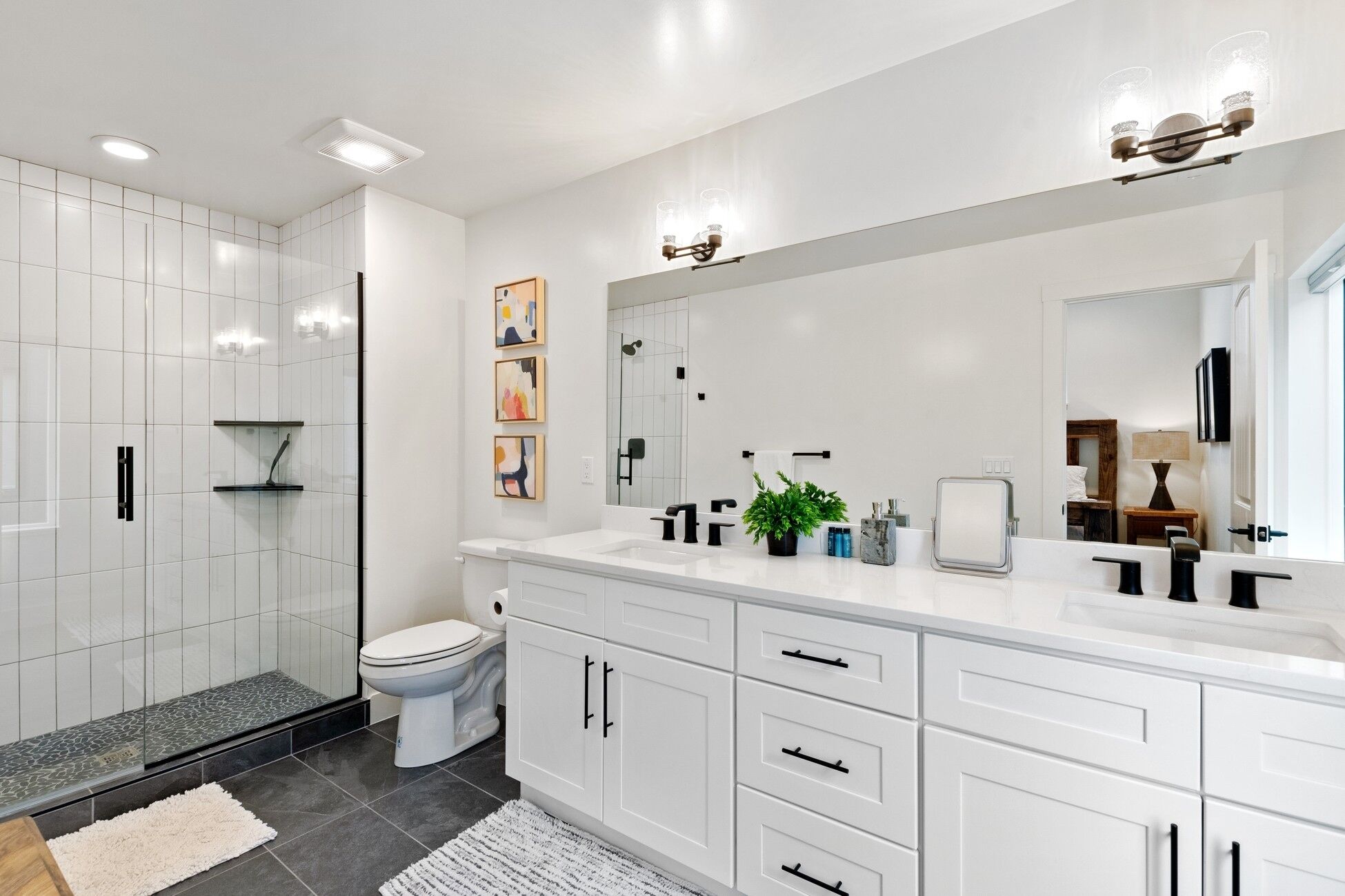 Une salle de bain moderne dotée d’une douche à l’italienne, de toilettes et d’un grand meuble-lavabo avec des tiroirs et un miroir.