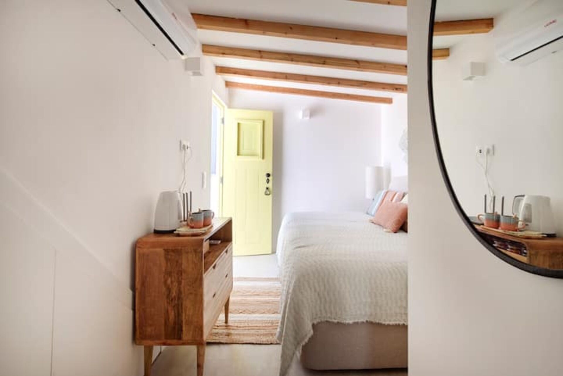 A bedroom with a bed, a wooden dresser, a mirror, and a door leading to another room.