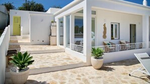 Un edificio moderno blanco con un patio cubierto, asientos exteriores y plantas en macetas.
