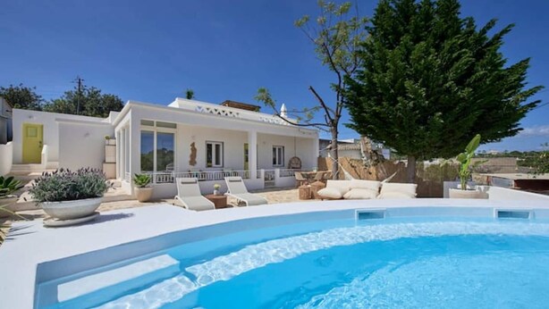 Una villa moderna con piscina, mobiliario exterior y un gran árbol.