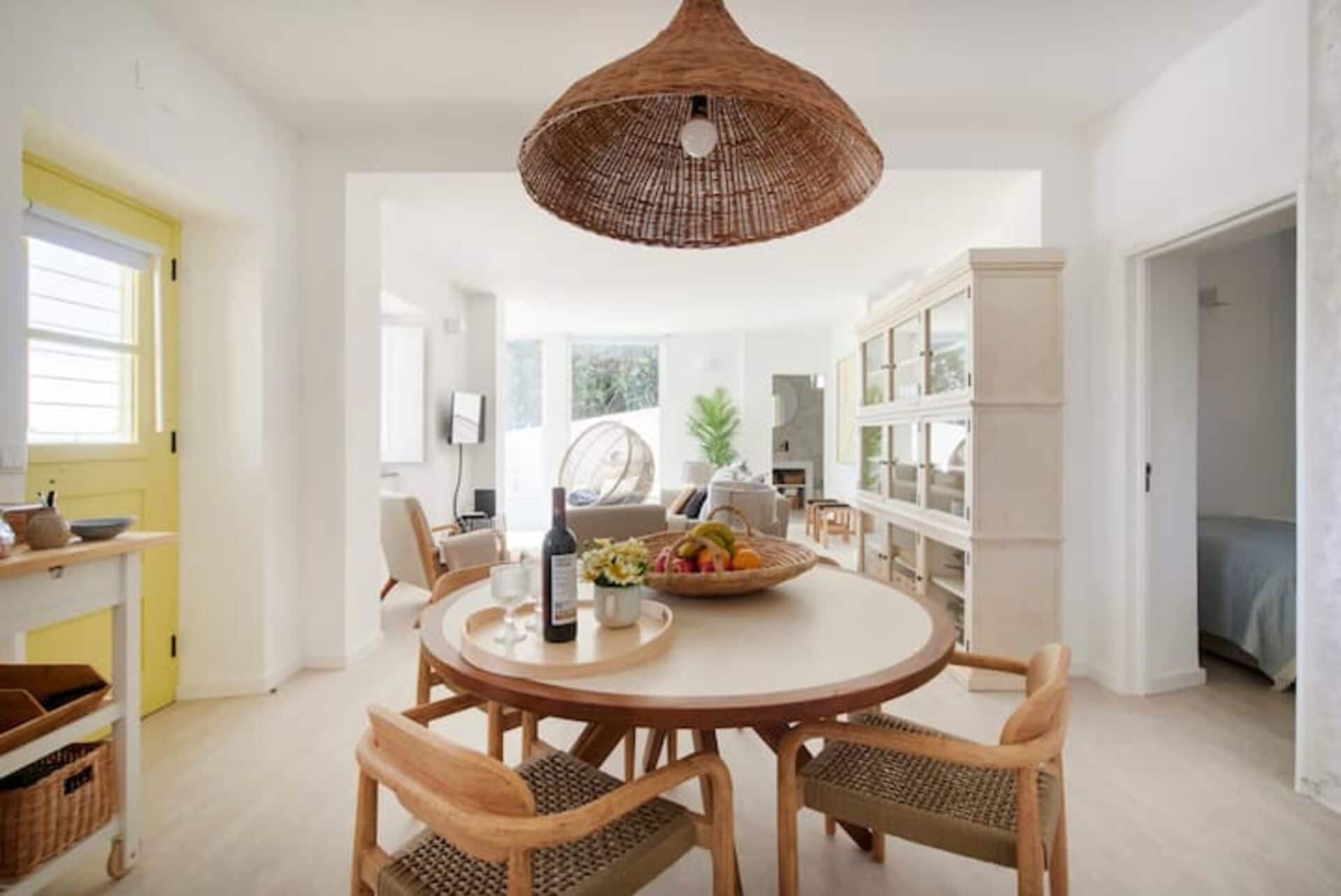A spacious dining area with a round table, wicker chairs, and a hanging light fixture.