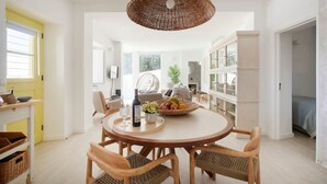 Un comedor espacioso con una mesa redonda, sillas de mimbre y una lámpara colgante.