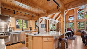 Une cuisine spacieuse dotée de meubles en bois, d’un grand îlot central et d’un coin repas offrant une vue sur l’extérieur.