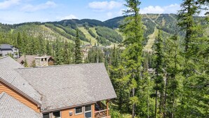 Une cabane en bois dotée d’un balcon donnant sur une vallée boisée et sur des montagnes lointaines.