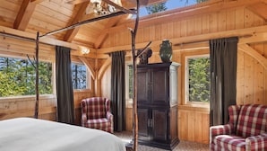 Une chambre dans une cabane en bois, avec un lit, deux fauteuils à carreaux, une armoire et une grande fenêtre.