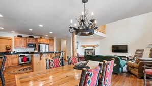 A spacious living area with a wooden dining table, colorful chairs, a green sofa, and a fireplace.