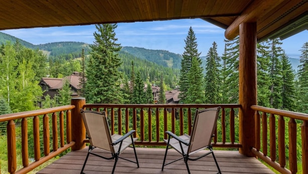 A wooden deck with two chairs and a view of a forested mountain area.