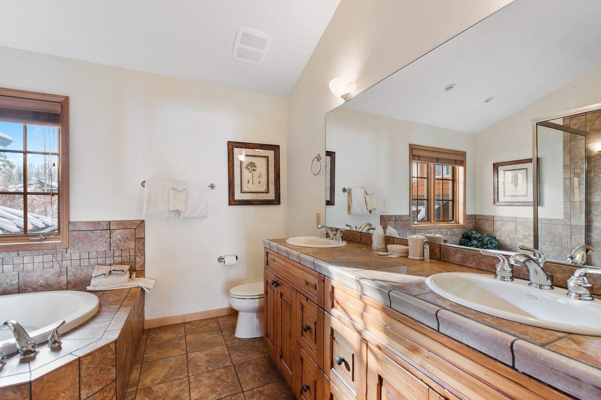 A bathroom with two sinks, a toilet, and a bathtub. There are wooden cabinets and a large mirror.